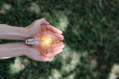 Hand hält leuchtende Glühbirne vor grünem Hintergrund – Symbol für Energiespartipps und nachhaltigen Stromverbrauch