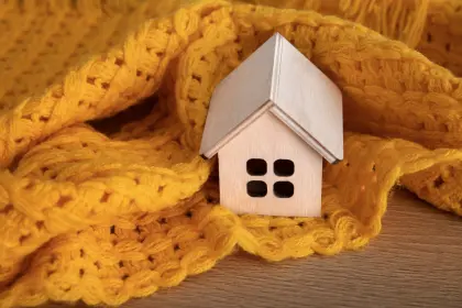 Kleines Holzhaus eingewickelt in gelbe Strickdecke – Symbol für klimaneutrale und effiziente Fernwärme der EV Greiz