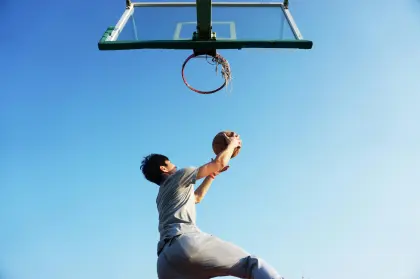 Ein Basketballer fängt seinen Ball im Sprung, der gerade im Korb gelandet ist.