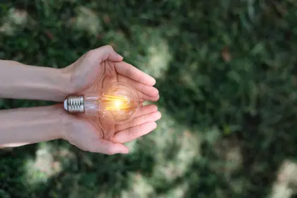 Hand hält leuchtende Glühbirne vor grünem Hintergrund – Symbol für Energiespartipps und nachhaltigen Stromverbrauch