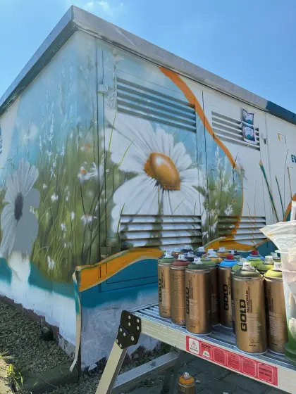 Graffitti-Sprühflaschen stehen vor einer gestalteten Trafostation.