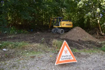 Ein gelber Bagger steht hinter einem Erdhaufen und davor ein Warndreieck mit der Aufschrift "Arbeiten an Gasleitungen".
